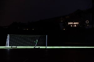 Ein Fußballtor auf einem Dunklen Spielfeld. Ein Leuchtschild zeigt BRD–DDR 1:0.