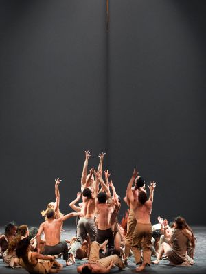 A group of dancers stretch their hands towards a rope hanging above them.