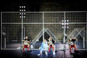 Performers with drums in front of a barred fence