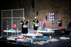 Performers with drums stand on camp beds and a platform