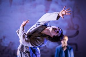 A dancer bends backwards and stretches his arms into the air.