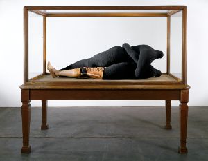 Eine Textilskulptur aus zwei menschlich anmutenden Figuren in einer Vitrine