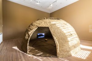 The exhibition view shows a dome-structure made of clay, in which a screen is placed.