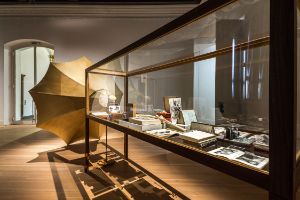 Das Foto zeigt den Ausstellungsraum, in dem eine Glasvitrine gefüllt mit unterschiedlichen Objekten steht, von dem ein großer Grammophon-Trichter wegführt.