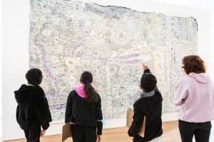 Vier jugendliche Personen, die mit dem Rücken zur Kamera vor einem Kunstwerk stehen.
