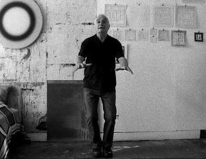 Filmstill aus Rirkrit Tiravanijas "untitled 2008 (john giorno reads)", auf dem der Künstler John Giorno in die Kamera gestikuliert.
