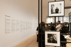 Ein schwarzes Gittersystem mit Schwarz-Weiß-Fotografien der Fotografin Diane Arbus in den Ausstellungsräumen des Gropius Bau. Zwischen den Stellagen sind Besuchende, die sich die Fotografien anschauen.