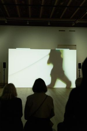 Ein Gruppen an Menschen Blickt auf eine Leinwand vor sich. Zu sehen ist eine Szenen einer Performance.