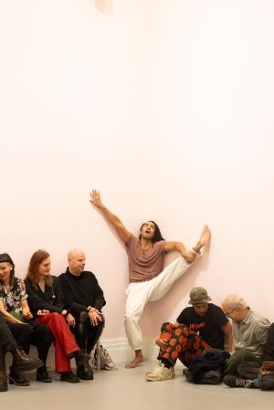 In einem hellrosa gestrichenen Raum findet eine Live-Performance mit dem Titel „study now steady“ statt. Eine Person bewegen sich dynamisch durch den Raum. Das Publikum sitzt auf einfachen Bänken und beobachtet aufmerksam das Geschehen.