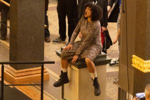 Das volle Atrium des Gropius Bau, bei der Eröffnung der Ausstellung Ligia Lewis: Ligia Lewis: I’M NOT HERE FORRRRR… In der MItte der Besuchenden sitzt eine performenen Person auf einem Sockel.