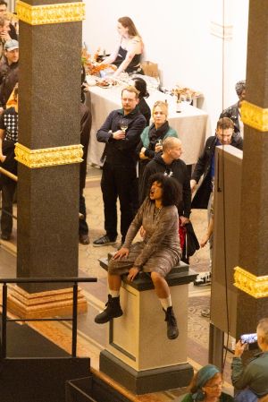 Das volle Atrium des Gropius Bau, bei der Eröffnung der Ausstellung Ligia Lewis: Ligia Lewis: I’M NOT HERE FORRRRR… In der MItte der Besuchenden sitzt eine performenen Person auf einem Sockel.