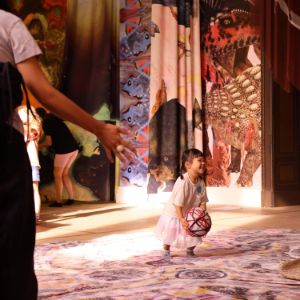 Ein Kind, das mit einem Ball in einem Raum mit bunten Tapeten und Teppichen spielt.