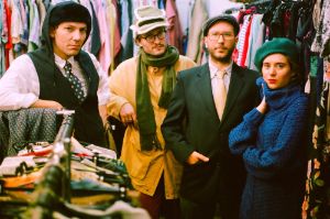 Musicians from the quartet Lumpeks, standing next to each other between racks of clothes and looking into the camera.