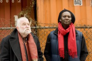 Die Musiker Peter Brötzmann und Hamid Drake stehen vor einem Bauzaun.
