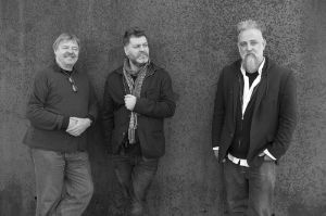 John Surman, Mat Maneri und Lucian Ban, die Mitglieder des Trios Transylvanian Folk Songs, stehen vor einer Mauer.