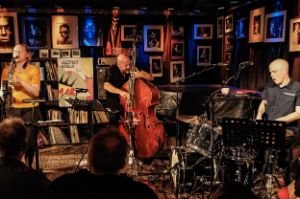 Auf einer kleinen Bühne, links Mette Rasmussen am Saxophon, mittig Ingebrigt Håker Flaten am Kontrabass, rechts Chris Corsano am Schlagzeug.