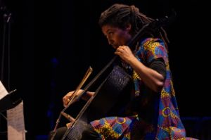 Die Musikerin blickt konzentriert auf ihre Noten und streicht mit dem Bogen über die Saiten ihres Cellos.