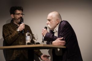 Links Musikjournalist Margasak, rechts der Musiker Brötzmann. Letzter lehnt sich auf einen Tisch, beide halten ein Mikrophon in den Händen.