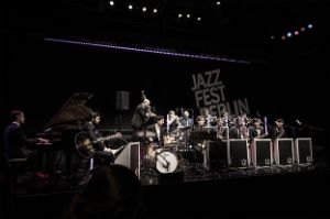 14 Musiker*innen auf der umgebauten Bühne des Festspielhauses, im Hintergrund ist der Schriftzug „Jazzfest Berlin“ als Projektion sichtbar.
