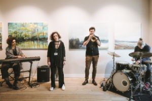 Vier Musiker*innen in einer Galerie, im Hintergrund hängen Bilder mit impressionistischen Landschaftsbildern.