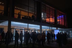People stand in front of and inside the illuminated Haus der Berliner Festspiele. It is dark outside.