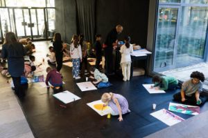 Viele Kinder malen am Boden der Kassenhalle des Haus der Berliner Festspiele Bilder mit Acrylfarbe.