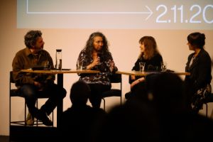 Angelica Sanchez speaks into a mike. Beside her sit Peter Margasak, Marilyn Crispell and Nadin Deventer