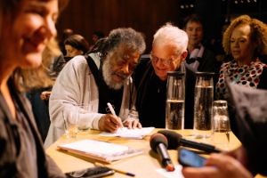 Wadada Leo Smith signs autographs at a standing table surrounded by several people.