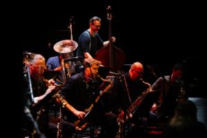 A group of brass players dynamically lean forward in sync while playing.