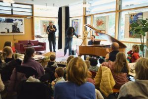 In a bright room, a trio plays for an audience consisting of people of different ages.