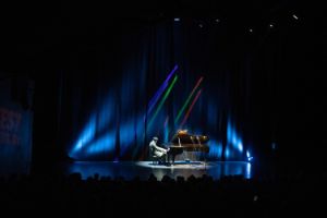 View from a distance to a stage that is empty apart from Pat Thomas playing the grand piano