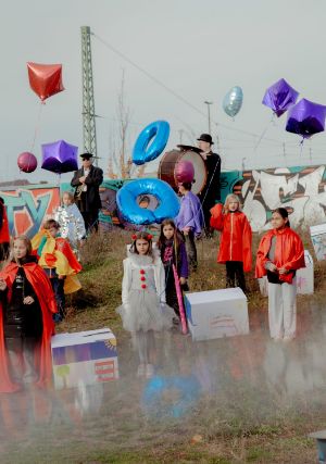 Kinder in bunten clownesken Kostümen im Freien. Sie halten große verschiedenförmige Ballons.