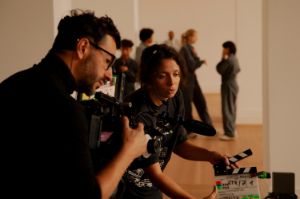 Eine Person filmt mit einer Kamera, eine andere hält die Filmklappe vor die Linse.