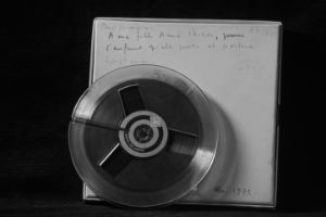 Magnettonbandspule mit der Aufnahme der Komposition Biogenesis von Élaine Radigue vor der dazugehörigen beschrifteten Aufbewahrungbox