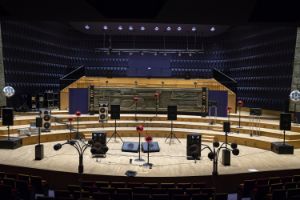 Several loudspeakers in different shapes and sizes are placed on a large stage. The auditorium is empty.