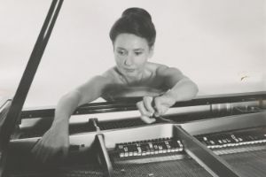 Lucia Dlugoszewski stands at an open piano and picks the strings.