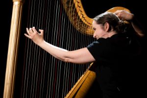 Musikerin Gunnhildur Einarsdóttir beim Spielen der Harfe während einer Aufführung. Sie trägt ein dünnes Headset-Mikrofon.