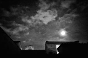 Über einem Hausdach leuchtet hell der Mond.