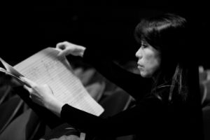 A seated woman holds a large score in her hands