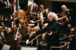Sir Simon Rattle conducts, with the orchestra around him.