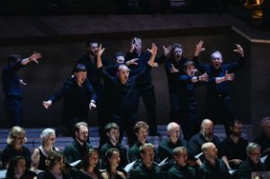 The choir is lined up in two rows, a few steps above, other choir members gesticulating wildly.