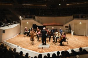 Sir George Benjamin conducts the colourfully dressed ensemble with his back to the audience.