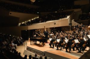 Side view of the stage with the orchestra, rows of audience in front and behind.