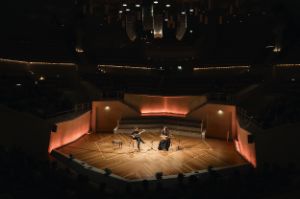 The two musicians play on the otherwise empty stage , the auditorium is dark.