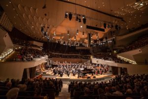 Ein voll besetzter Konzertsaal mit einem großen Orchester und einem Konzertflügel auf der Bühne.