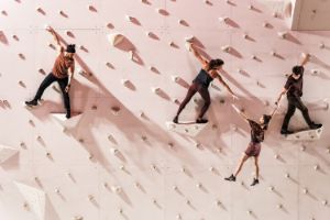 Performers are on a climbing wall.