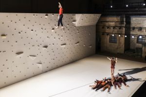 A performer balances over a rope, below him a performer stands on the hands of other performers.