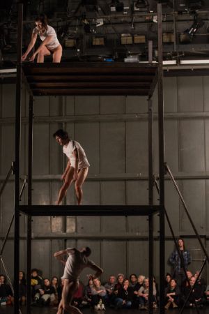 Three dancers dressed in T-shirts are on different levels of a three-storey open scaffold.