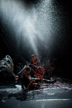 Dimitris Papaioannou performt mit einem Wasserschlauch und einem Kraken-Requisit.