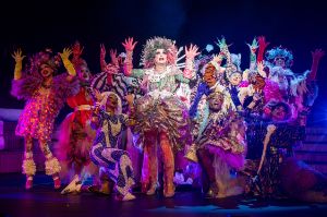A group of people in garish, colourful clothing raise their hands in the air.